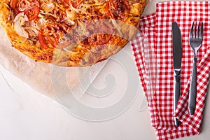 Hot homemade pizza with chicken meat, tomatoes, onions near with cutlery fork and knife on red tablecloth, flat lay, top view