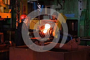 Blacksmith processes the iron product under a huge press, forging metal, stamping.