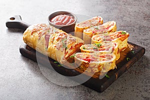 Hot Italian stromboli roll stuffed with salami sausage and mozzarella cheese close-up on a wooden board. horizontal