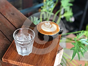 Hot latte coffee in Black cup and water glass on the vintage wooden table with natural light.