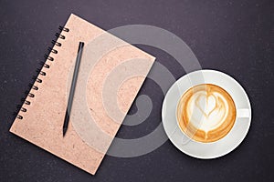 Hot latte coffee in white cup and notebook with blank empty cove