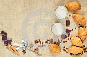 Hot latte or mocaccino decorated with coffee beans, croissants, chocolate, spices and vintage spoons on the brown cloth background