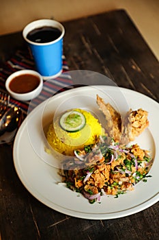 Hot Lemony Chicken Rice Meal served in plate with sauce, cold drink, spoon and fork isolated on wooden board side view of thai
