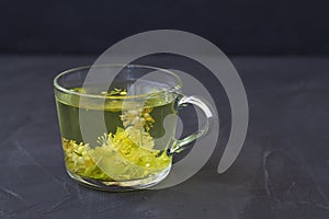 Linden flowers tea.Cup of hot herbal tea with linden fresh flowers on a black table