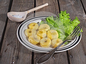 Hot lunch of potato gnocchi with leaves of fresh leaf lettuce on a ceramic plate with stripes, shot from close range on a plank