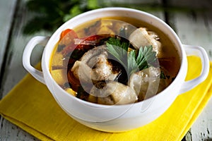 Hot meat soup with dumplings, pumpkin and fresh herbs in a beautiful white plate on a wooden table