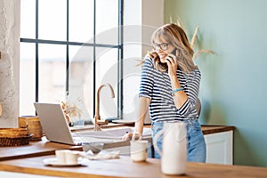 Hot of middle aged woman using mobile phone and laptop while working from home