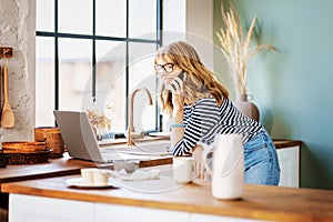 Hot of middle aged woman using mobile phone and laptop while working from home