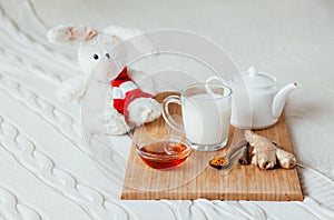 Hot milk in a glass cup and honey on wooden board. Treatment of children drink. folk remedies in bed. Soft toy