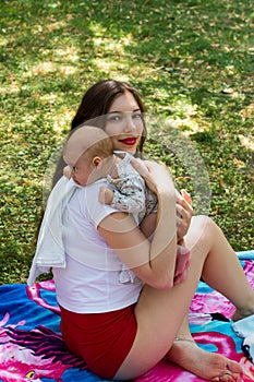 Hot mom and a cute baby in the park, young lady and new mother holding an infant in loving arms with head on the shoulder to burp