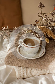 Hot mug of cappuccino on wooden tray on the bed, breakfast, bouquet of dried flowers. Spring scenery. Cozy house. Beige natural