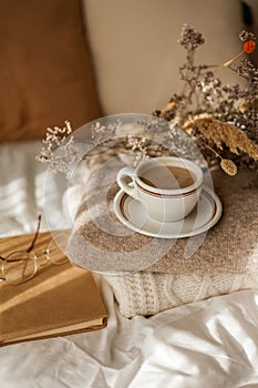 Hot mug of cappuccino on wooden tray on the bed, breakfast, bouquet of dried flowers. Spring scenery. Cozy house. Beige natural