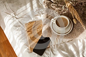 Hot mug of cappuccino on wooden tray on the bed, breakfast, bouquet of dried flowers. Spring scenery. Cozy house. Beige natural