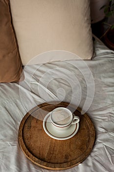 Hot mug of cappuccino on wooden tray on the bed, breakfast. Cozy house. Beige natural colors. Aesthetic