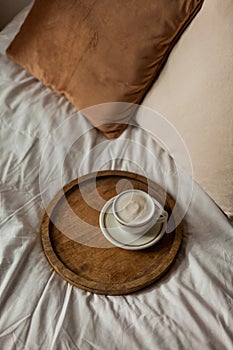 Hot mug of cappuccino on wooden tray on the bed, breakfast. Cozy house. Beige natural colors. Aesthetic