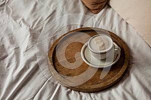 Hot mug of cappuccino on wooden tray on the bed, breakfast. Cozy house. Beige natural colors. Aesthetic