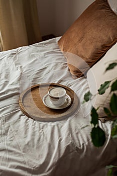 Hot mug of cappuccino on wooden tray on the bed, breakfast. Cozy house. Beige natural colors. Aesthetic