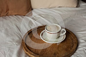 Hot mug of cappuccino on wooden tray on the bed, breakfast. Cozy house. Beige natural colors. Aesthetic