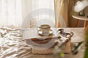 Hot mug of cappuccino on wooden tray on the bed, breakfast. Cozy house. Beige natural colors. Aesthetic