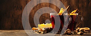 Hot mulled red wine cups with spices and fruits on wooden rustic table. Traditional Autumn hot drink, copy space