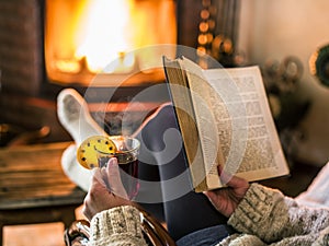 Hot mulled wine and book in woman hands. Relaxing in front of burning fire in the cold winter day