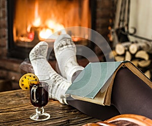 Hot mulled wine and book in woman hands. Relaxing in front of burning fire in the cold winter day