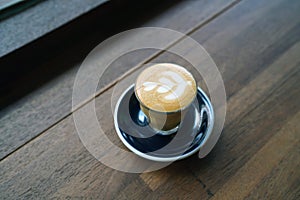 Hot Piccolo Latte - A glass of coffee with milk and beautiful leaf pattern latte art on wooden table and copy space.