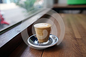 Hot Piccolo Latte - A glass of coffee with milk and beautiful leaf pattern latte art on wooden table and copy space, Perfect for