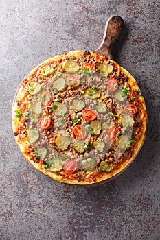 Hot pizza with ground beef, tomatoes, pickled cucumbers and cheese close-up on a wooden board. Vertical top view