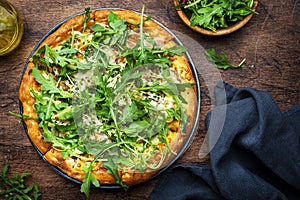 Hot pizza with mozzarella cheese, ham, pesto sauce and fresh arugula, rustic wooden table background, top view