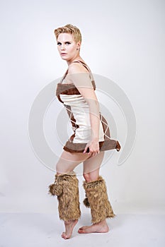 Hot plus size woman in fur carnival costume of primitive man on white background in Studio. a beautiful savage girl in a brown dre