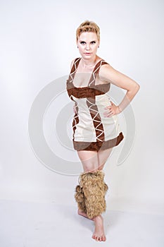 Hot plus size woman in fur carnival costume of primitive man on white background in Studio. a beautiful savage girl in a brown dre