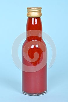 Hot red chilly sauce in little glass bottle on blue background.