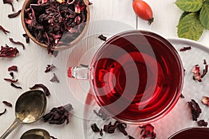 Hot red karkade tea in glass cups with dry tea on a white wooden table. Top view.