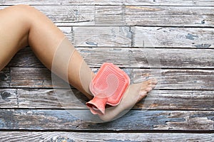 Hot red water bottle on woman ankle and foot pain on grungy wood, Health care