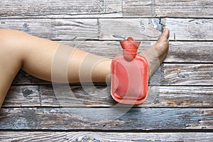 Hot red water bottle on woman ankle and foot pain on grungy wood, Health care