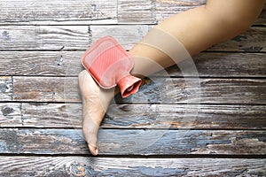 hot red water bottle on woman ankle and foot pain on grungy wood, remedy for pains concept