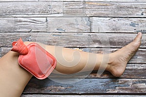 Hot red water bottle on woman knee to healing pain on grungy wood, remedy for pains concept