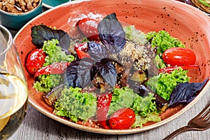 Hot salad with grilled tomatoes, eggplant, zucchini, red pepper, salad leaves, garnished with grated walnuts and basil