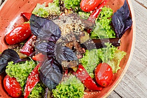 Hot salad with grilled tomatoes, eggplant, zucchini, red pepper, salad leaves, garnished with grated walnuts and basil