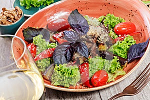 Hot salad with grilled tomatoes, eggplant, zucchini, red pepper, salad leaves, garnished with grated walnuts and basil and glass o