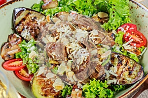 Hot salad with veal, mushrooms, salad leaves, eggplant, zucchini, tomatoes, garnished with grated almonds and Parmesan cheese