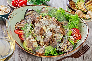 Hot salad with veal, mushrooms, salad leaves, eggplant, zucchini, tomatoes, garnished with grated almonds and Parmesan cheese and