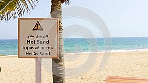 Hot sand sign in Arabic, English, Russian and German language. Hot summer beach with waves crashing in the background