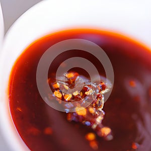 Hot sauce of red dry chili peppers with soy oil in a white bowl close-up