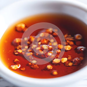 Hot sauce of red dry chili peppers with soy oil in a white bowl close-up