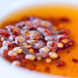 Hot sauce of red dry chili peppers with soy oil in a white bowl close-up