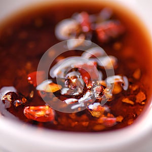 Hot sauce of red dry chili peppers with soy oil in a white bowl close-up