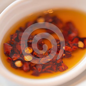 Hot sauce of red dry chili peppers with soy oil in a white bowl close-up