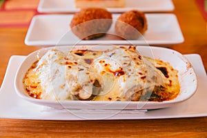 Hot served Lasagne in white plate with Papas Rellenas in background. Spanish and Latin America dish photo